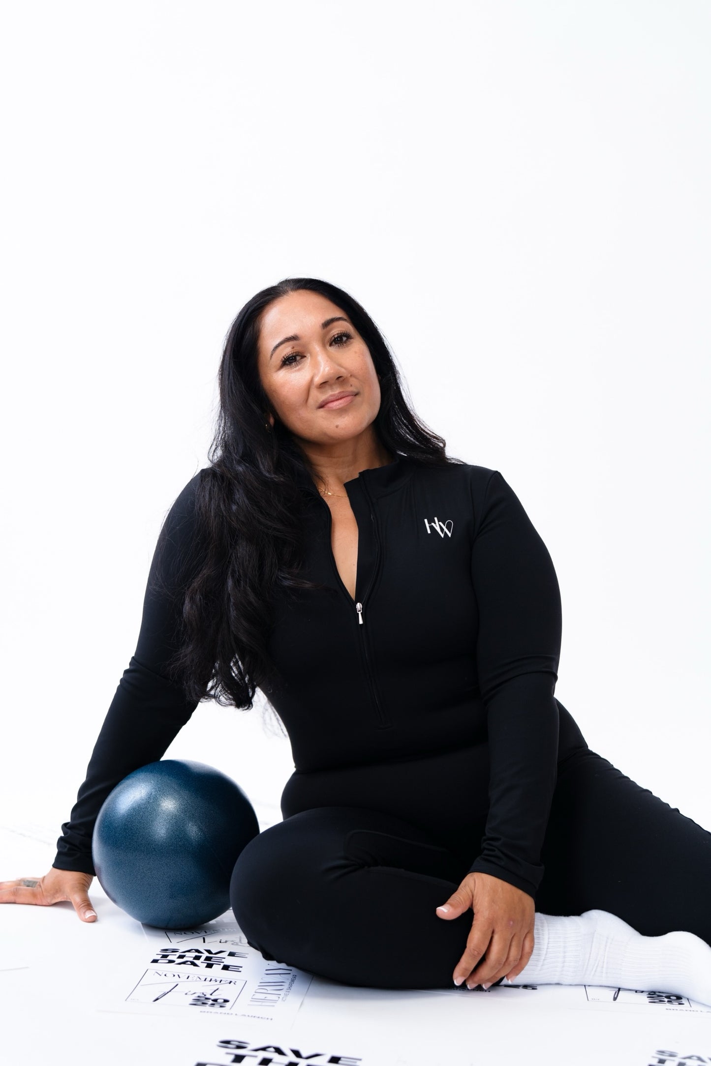 Woman in black athletic wear sitting on a white background with a blue exercise ball.